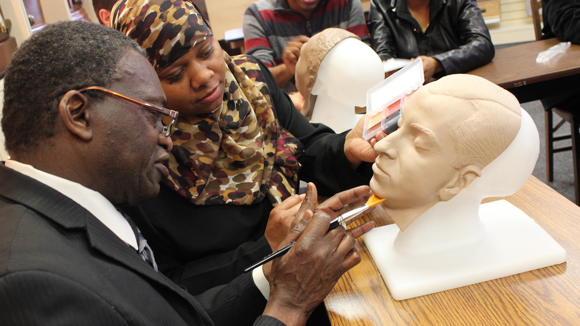 Funeral service students practice applying color to mannequin heads