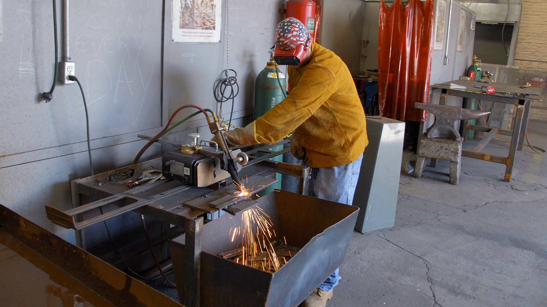 Welding student practices cutting metal in workshop with sparks flowing