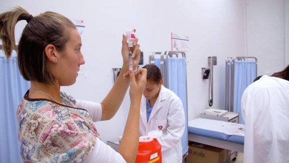 medical student practices taking liquid from bottle using syringe