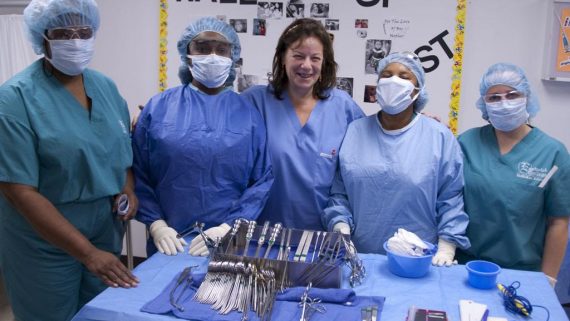 Medical students pose with instructor in front of table full of medical tools